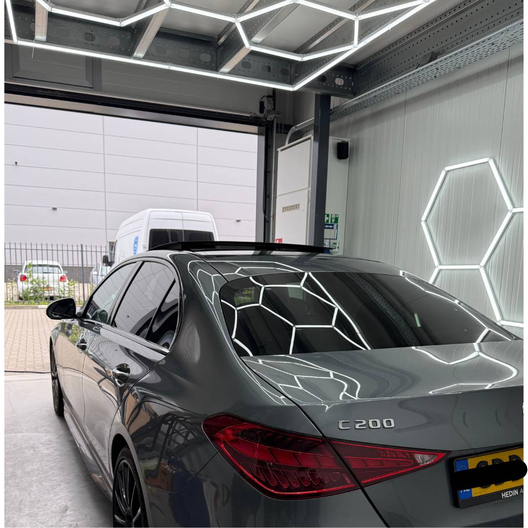 Achterkant van een auto in de verlichte werkplaats met een geopende roldeur.